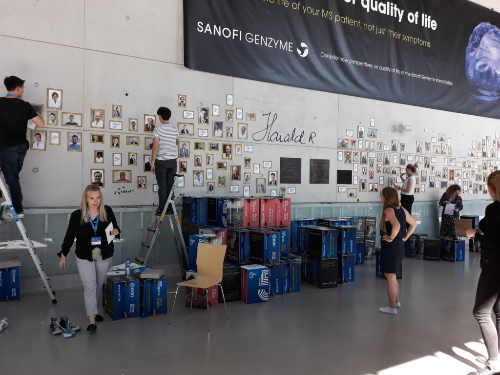 People placing pictures on a large wall, others standing and walking around