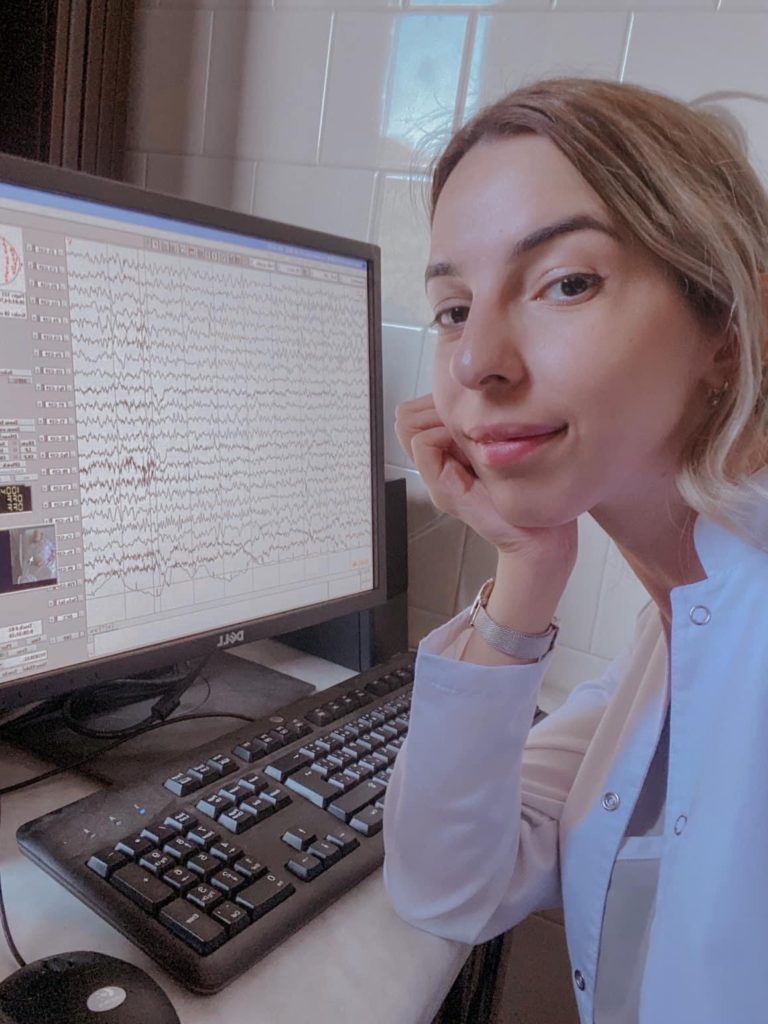 Woman posing in front of computer, one elbow leaniing on desk