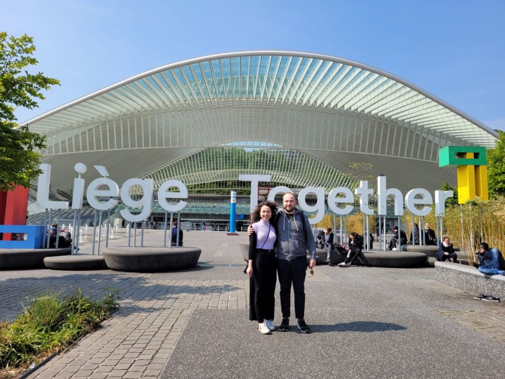 Two people posing in front of a large, modern building