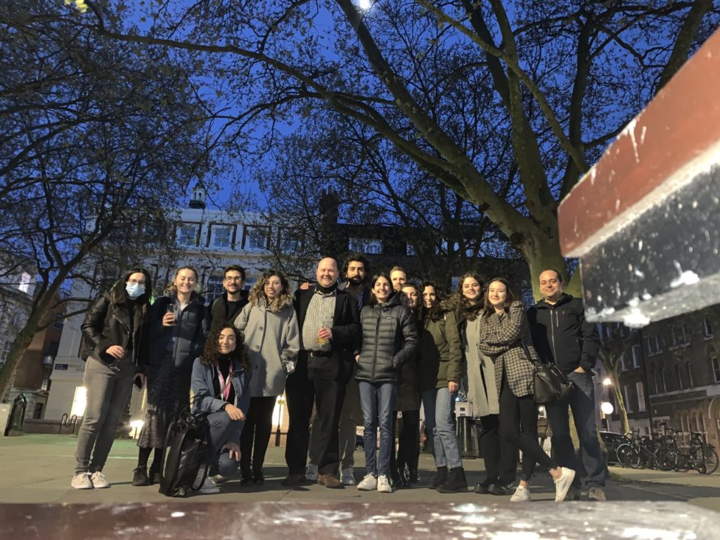 Group of people gathered together, posing for a photo under a tree, next to a university building at night