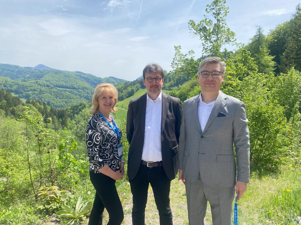 Three people posing outdoors with hills and trees in background